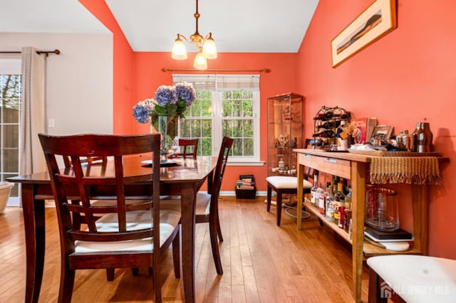 dining area with hardwood / wood-style flooring, a chandelier, lofted ceiling, and baseboards