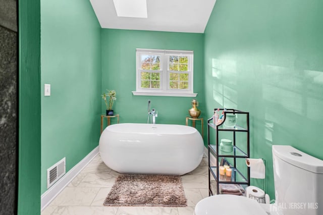 bathroom with marble look tile flooring, a skylight, toilet, a soaking tub, and baseboards