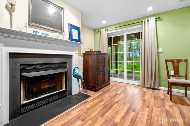 living area featuring a fireplace with flush hearth, wood finished floors, recessed lighting, and baseboards