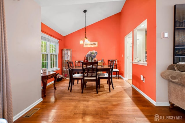 dining room featuring light wood-type flooring, baseboards, and high vaulted ceiling