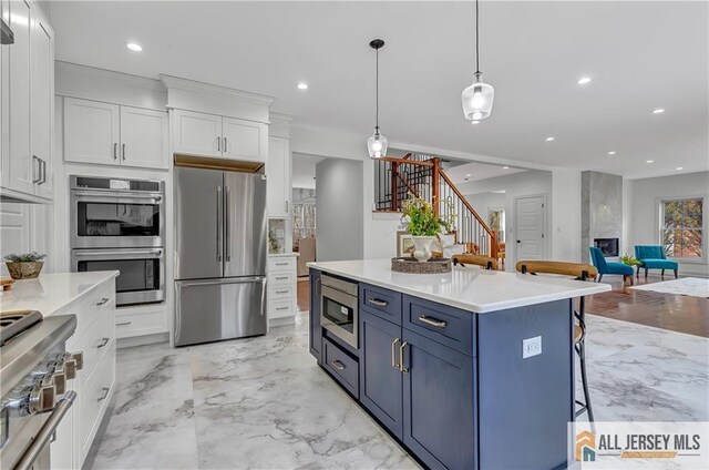 kitchen with appliances with stainless steel finishes, decorative light fixtures, blue cabinets, white cabinetry, and a kitchen breakfast bar