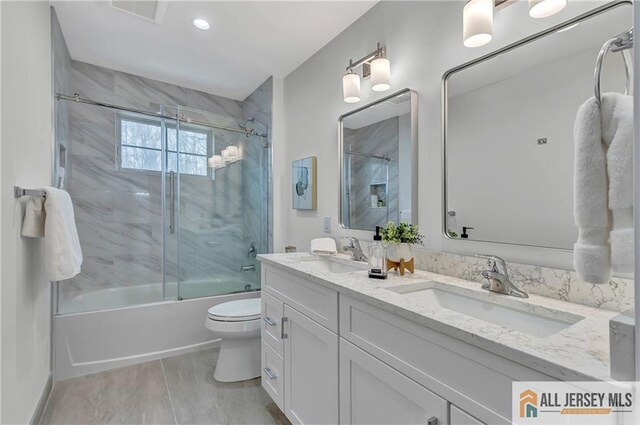 full bathroom with bath / shower combo with glass door, vanity, and toilet