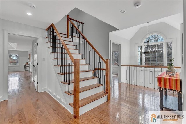 staircase with an inviting chandelier, lofted ceiling, and hardwood / wood-style floors