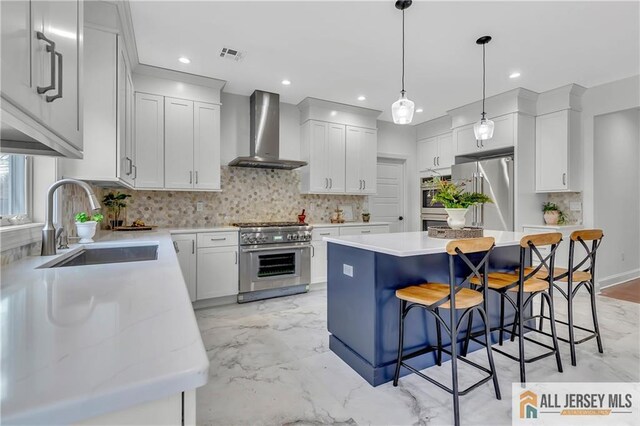 kitchen featuring wall chimney range hood, sink, white cabinetry, high quality appliances, and a kitchen island