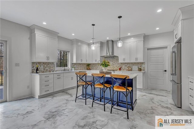 kitchen with high quality fridge, decorative light fixtures, white cabinets, a center island, and wall chimney range hood