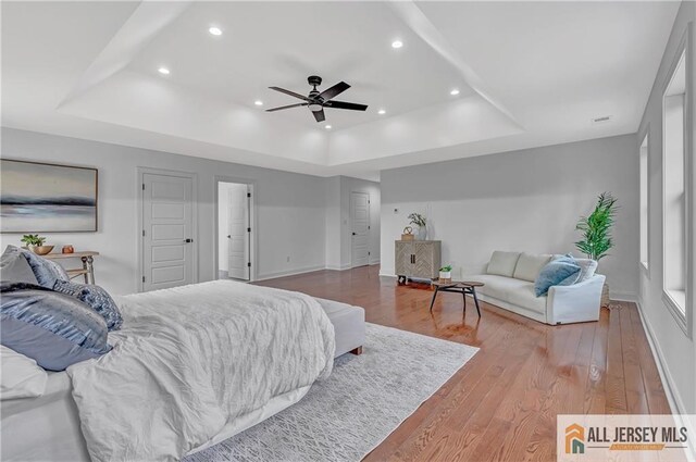 bedroom with hardwood / wood-style flooring, a raised ceiling, and ceiling fan