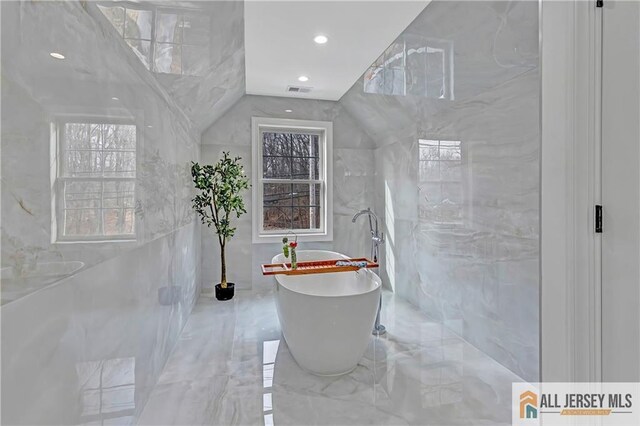 bathroom featuring vaulted ceiling, a washtub, and tile walls