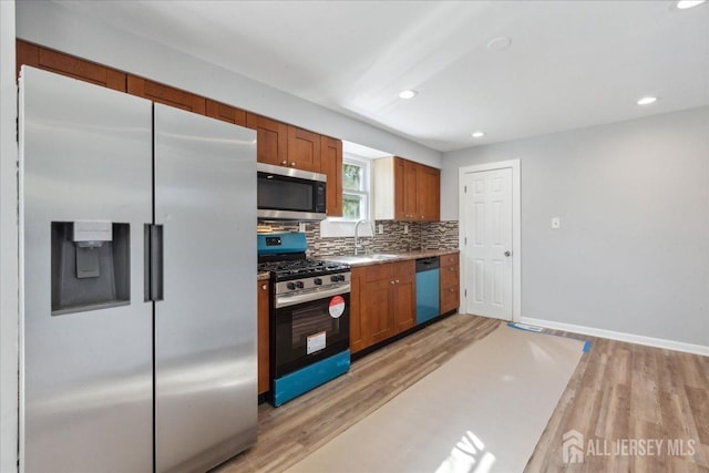 kitchen with appliances with stainless steel finishes, sink, backsplash, and light hardwood / wood-style floors