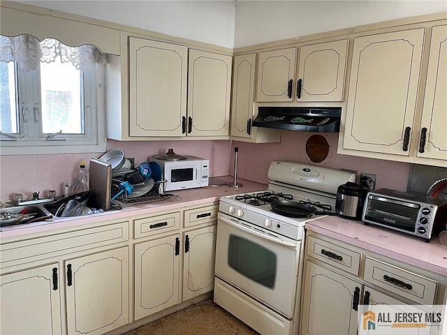 kitchen featuring under cabinet range hood, light countertops, cream cabinets, and white appliances