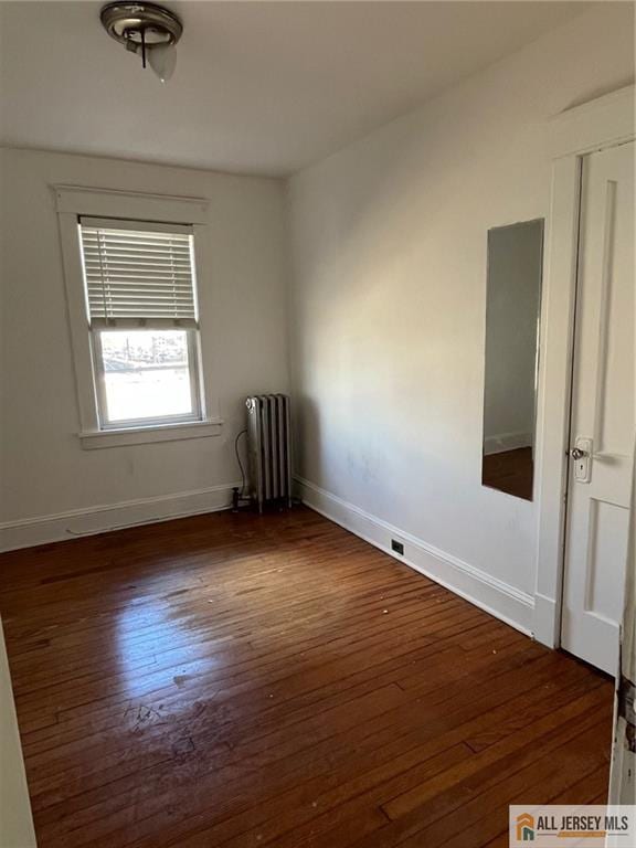 empty room featuring radiator, hardwood / wood-style flooring, and baseboards