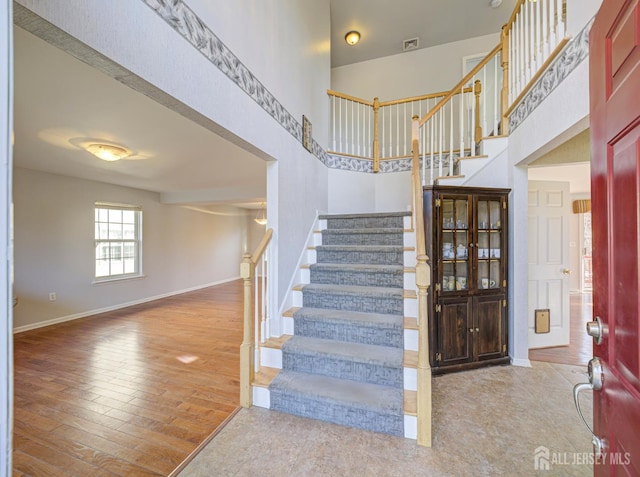 staircase with visible vents, wood finished floors, baseboards, and a towering ceiling