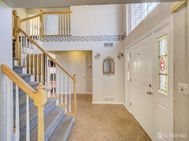 foyer entrance featuring visible vents, stairway, and a high ceiling