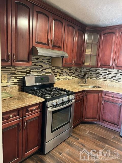 kitchen featuring dark wood finished floors, under cabinet range hood, stainless steel gas stove, and a sink
