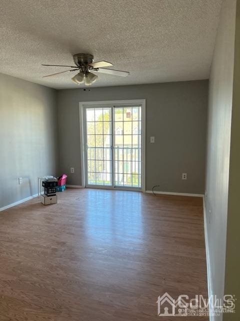 spare room featuring wood finished floors, a textured ceiling, baseboards, and ceiling fan