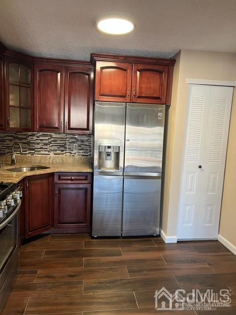 kitchen with tasteful backsplash, a sink, stainless steel refrigerator with ice dispenser, dark wood-style flooring, and gas stove