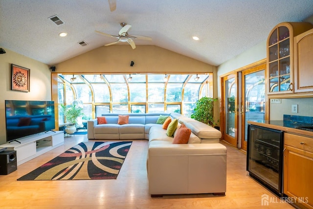 living room featuring a healthy amount of sunlight, light hardwood / wood-style flooring, beverage cooler, and vaulted ceiling