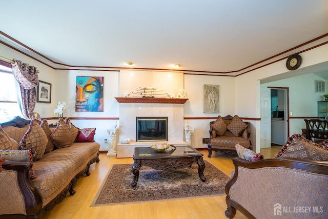 living room featuring a tile fireplace, light wood-type flooring, and ornamental molding