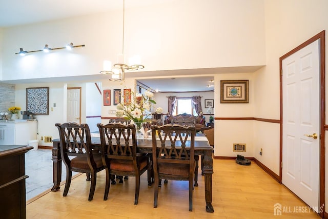 dining space featuring a towering ceiling, light hardwood / wood-style floors, and an inviting chandelier