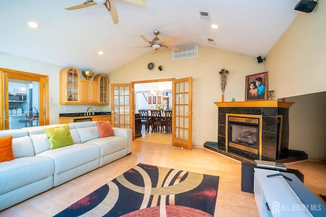 living room with french doors, sink, vaulted ceiling, light hardwood / wood-style flooring, and a fireplace