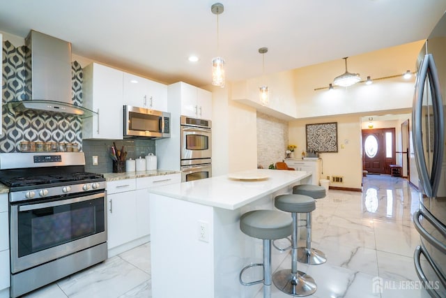 kitchen with white cabinetry, wall chimney exhaust hood, decorative light fixtures, a kitchen island, and appliances with stainless steel finishes