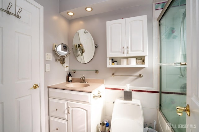 full bathroom featuring vanity, toilet, tile walls, and bath / shower combo with glass door