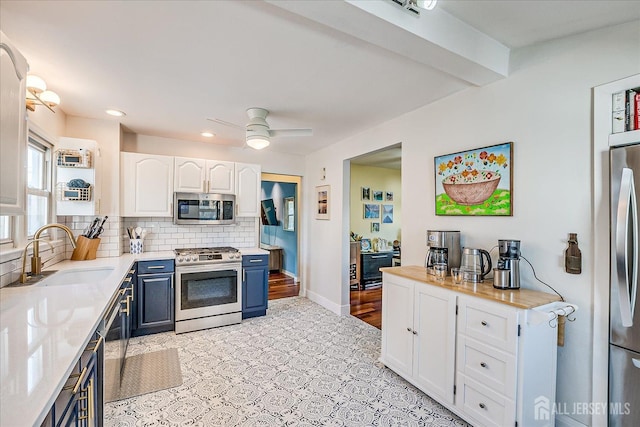 kitchen featuring appliances with stainless steel finishes, blue cabinetry, sink, white cabinetry, and backsplash