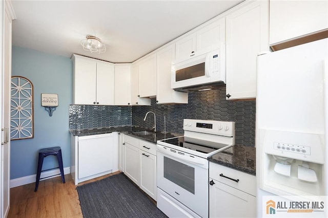 kitchen featuring white appliances, a sink, white cabinets, decorative backsplash, and dark stone countertops