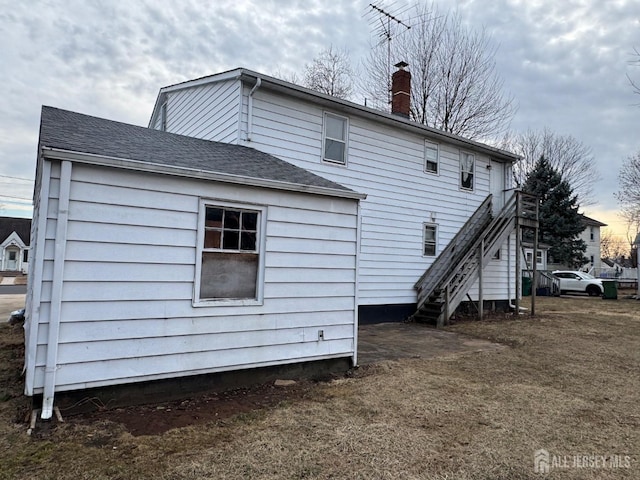 back of house featuring a chimney, stairs, and a shingled roof