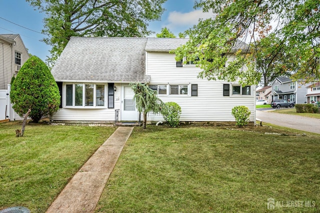 view of front facade with a shingled roof and a front lawn