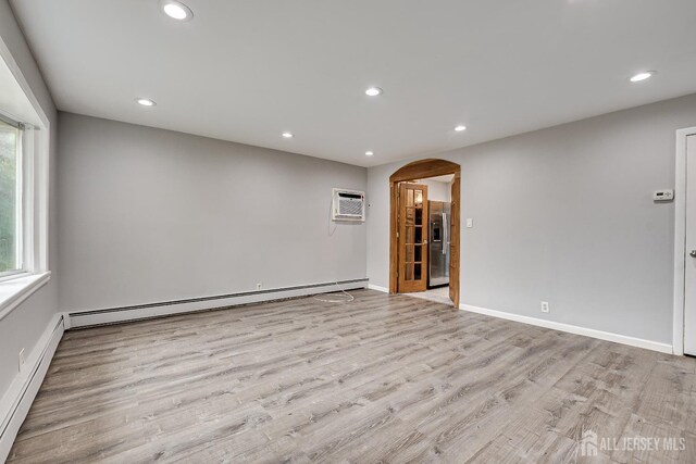 spare room featuring a baseboard radiator, a wall mounted air conditioner, and light hardwood / wood-style floors