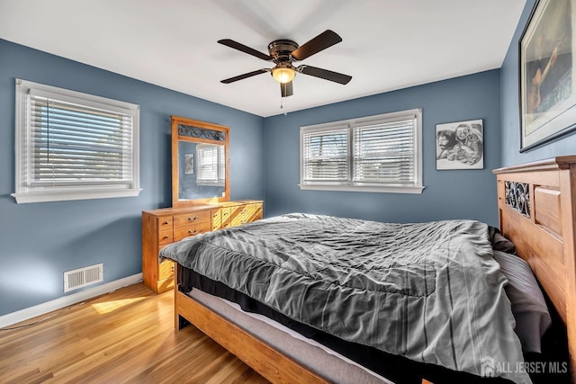 bedroom with a ceiling fan, wood finished floors, visible vents, and baseboards