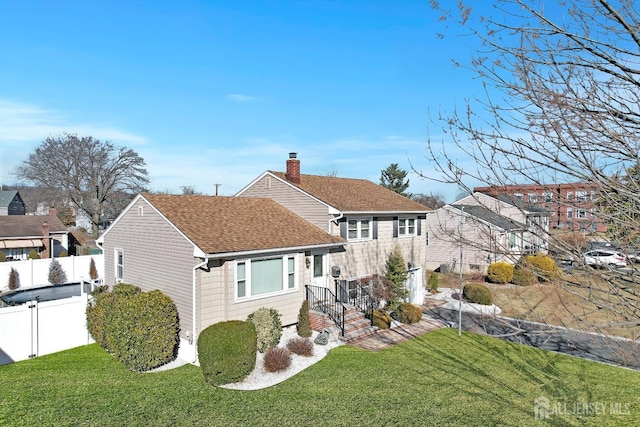 view of front of house featuring roof with shingles, fence, and a front yard