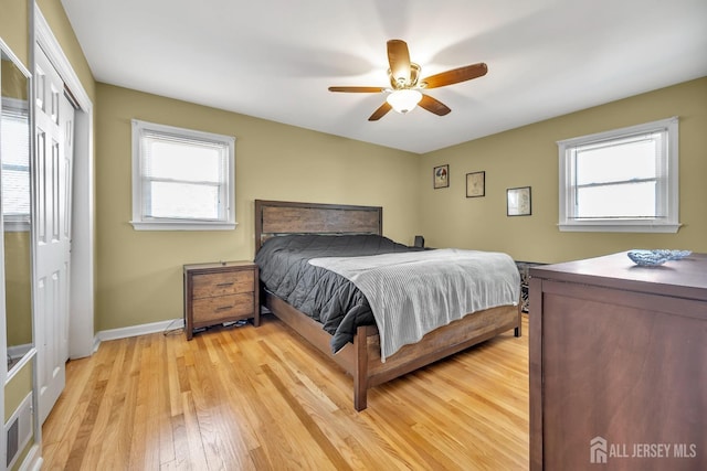 bedroom featuring a ceiling fan, a closet, light wood-style flooring, and baseboards