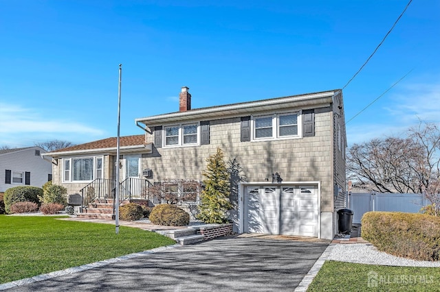 tri-level home with a chimney, aphalt driveway, an attached garage, fence, and a front lawn