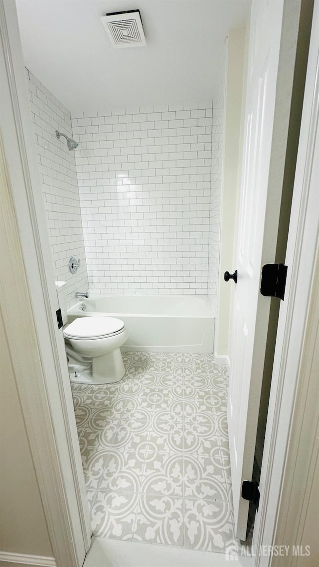 bathroom with tile patterned flooring, tiled shower / bath, and toilet