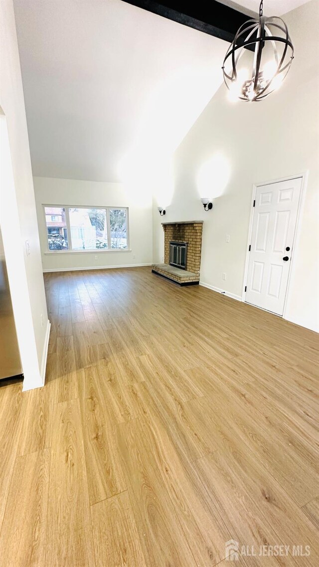 unfurnished living room with high vaulted ceiling, a chandelier, a brick fireplace, beamed ceiling, and light wood-type flooring