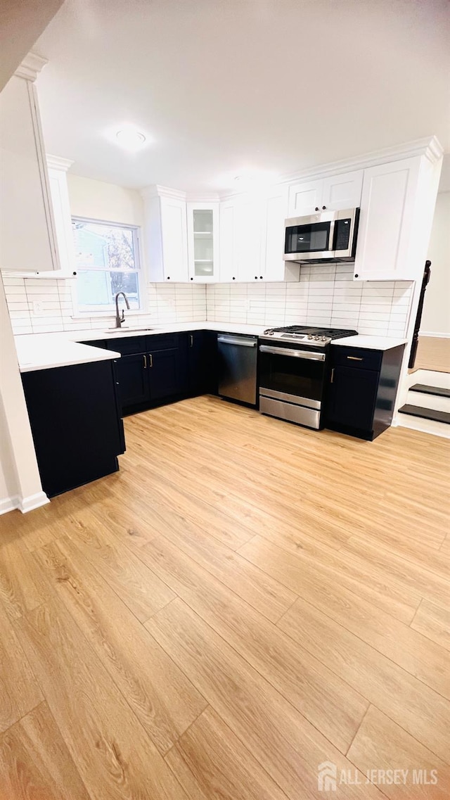 kitchen with sink, appliances with stainless steel finishes, white cabinets, light hardwood / wood-style floors, and backsplash