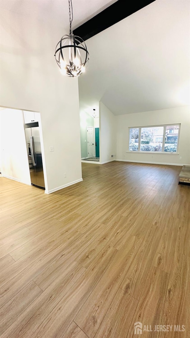 unfurnished living room with an inviting chandelier, light hardwood / wood-style floors, and vaulted ceiling with beams