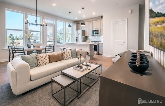 living room featuring recessed lighting, light wood finished floors, baseboards, and a notable chandelier
