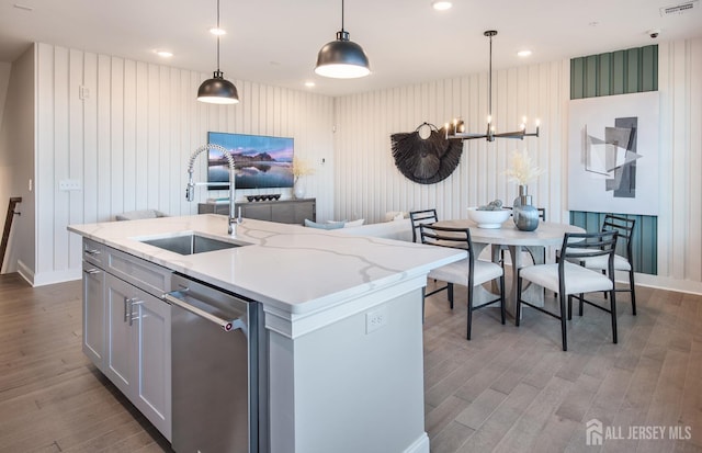 kitchen featuring hanging light fixtures, wood finished floors, dishwasher, a sink, and baseboards