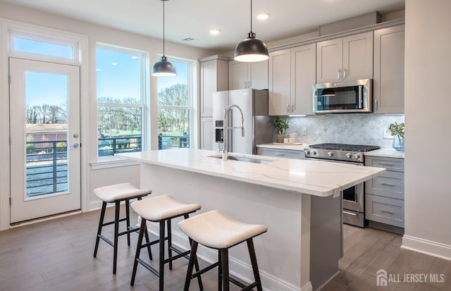 kitchen featuring backsplash, gray cabinetry, light wood-style floors, stainless steel appliances, and an island with sink