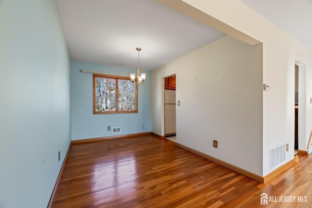 empty room with hardwood / wood-style floors and a notable chandelier