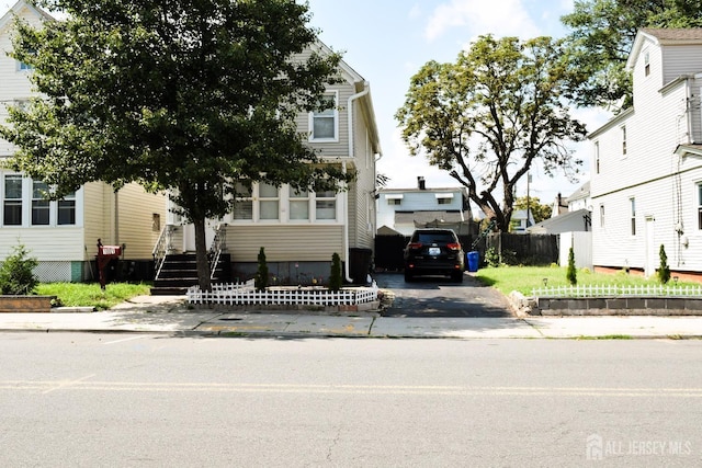 view of property hidden behind natural elements with driveway and fence