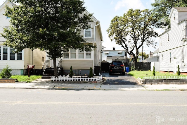 view of property hidden behind natural elements featuring driveway and fence