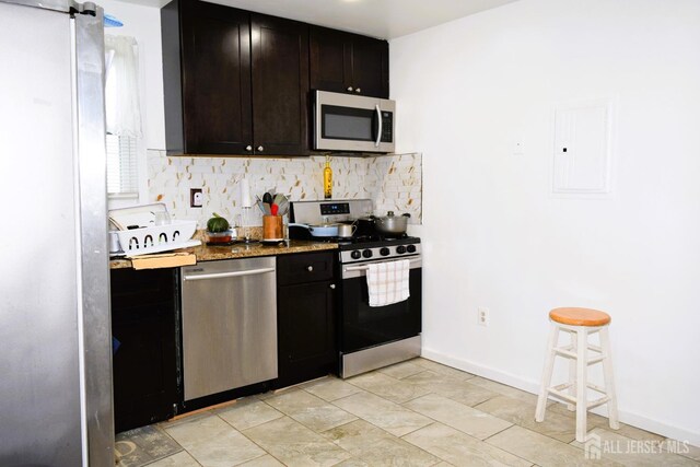 kitchen featuring dark brown cabinetry, appliances with stainless steel finishes, electric panel, dark stone counters, and decorative backsplash