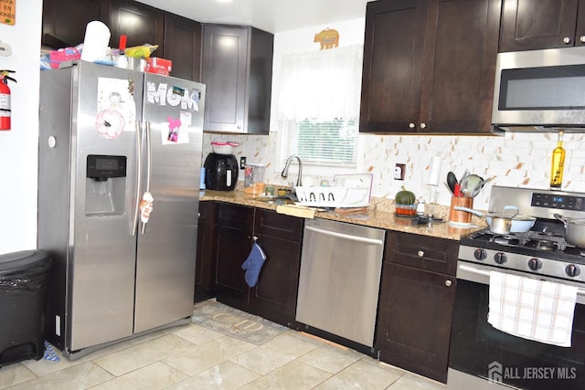 kitchen featuring light stone counters, dark brown cabinets, stainless steel appliances, and tasteful backsplash