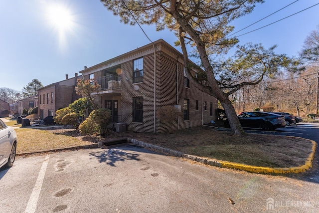 exterior space featuring uncovered parking, brick siding, central AC, and a balcony