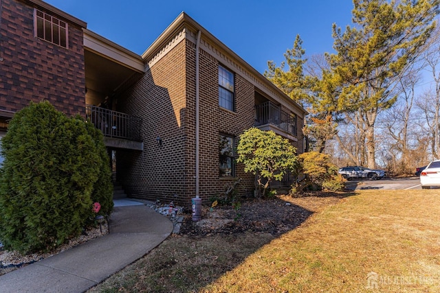 view of side of property featuring a yard, brick siding, and a balcony
