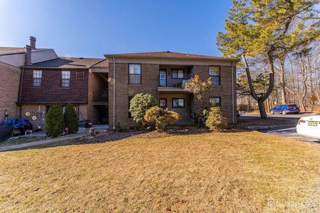view of front facade featuring brick siding, a front yard, and a balcony