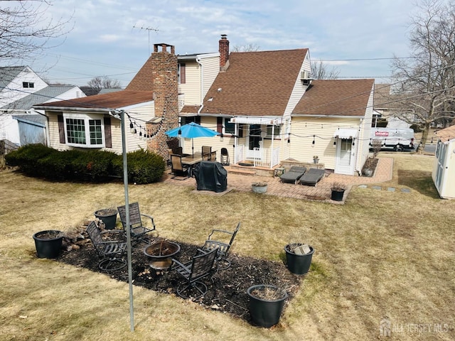 back of property featuring a lawn, a patio, fence, a fire pit, and a shingled roof